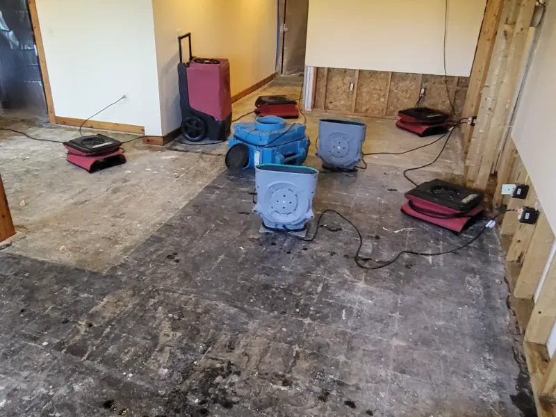 Industrial fans and air movers set up on a stripped floor in a partially renovated room.