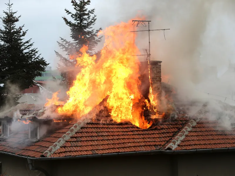 Flames and smoke engulf a tiled roof with a chimney and antenna.