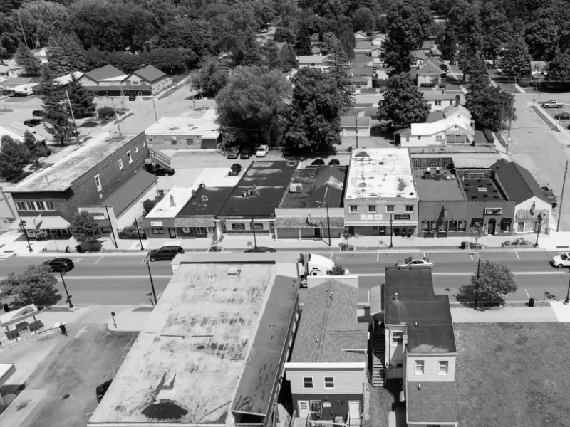 Aerial view of a small town street with parked cars and buildings on both sides.