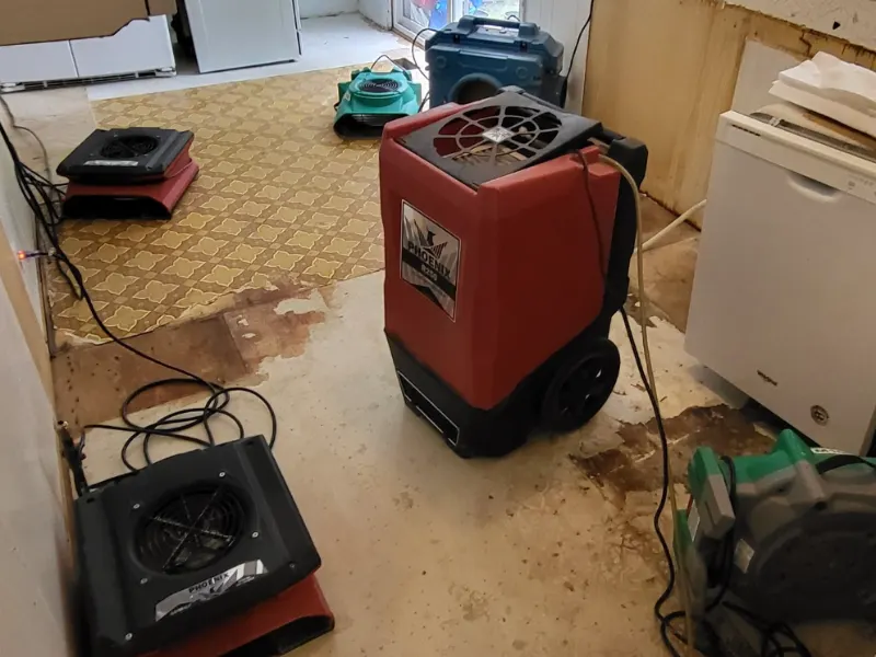A red industrial dehumidifier and several air movers on a partially stripped floor in a room.