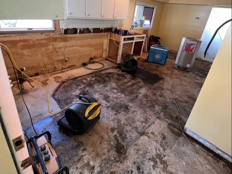 Room with water damage undergoing drying and restoration with fans and equipment on the floor.