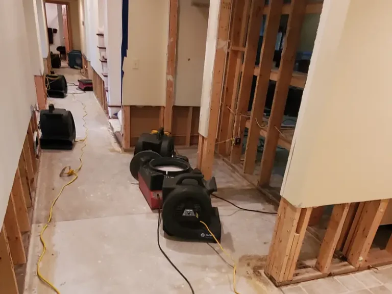 Multiple air movers and fans positioned in a hallway with walls partially stripped to studs.