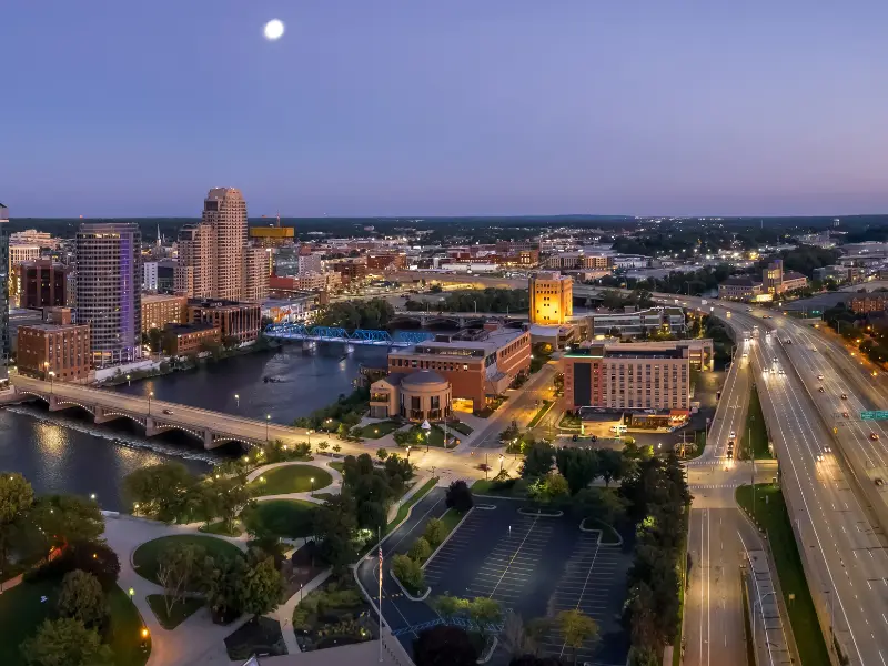 City skyline at dusk with a river, bridges, and illuminated buildings under a rising moon.
