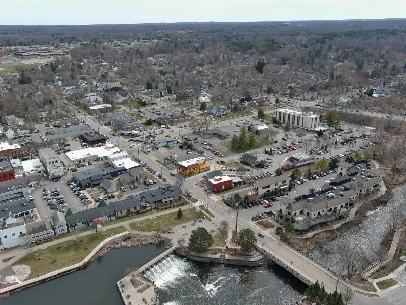 Aerial view of a small town with a river, dam, bridge, and clustered buildings.