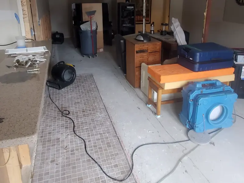 Room under renovation with furniture, a trash bin, and drying equipment on a dusty floor.