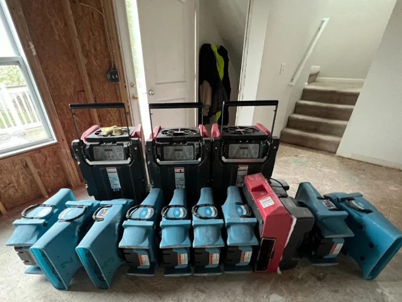 A row of blue and black industrial air movers and drying equipment lined up on a floor inside a room.