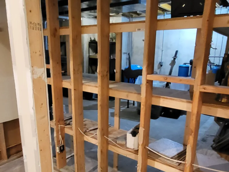 Exposed wooden wall studs with electrical wiring in an unfinished basement.