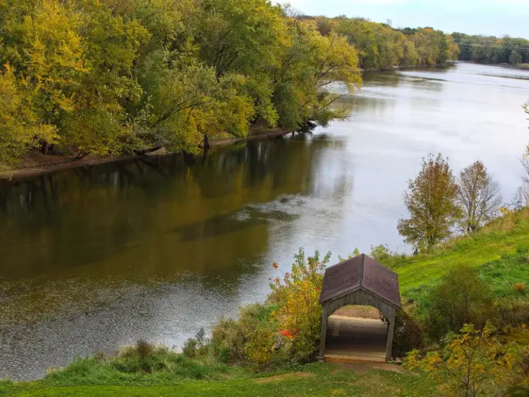 Covered wooden bridge over a river with trees showing autumn colors along the banks.