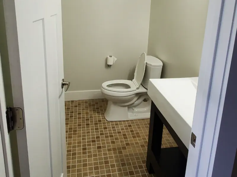 Bathroom with a white toilet, open lid, and a sink with a dark cabinet on a tiled floor.