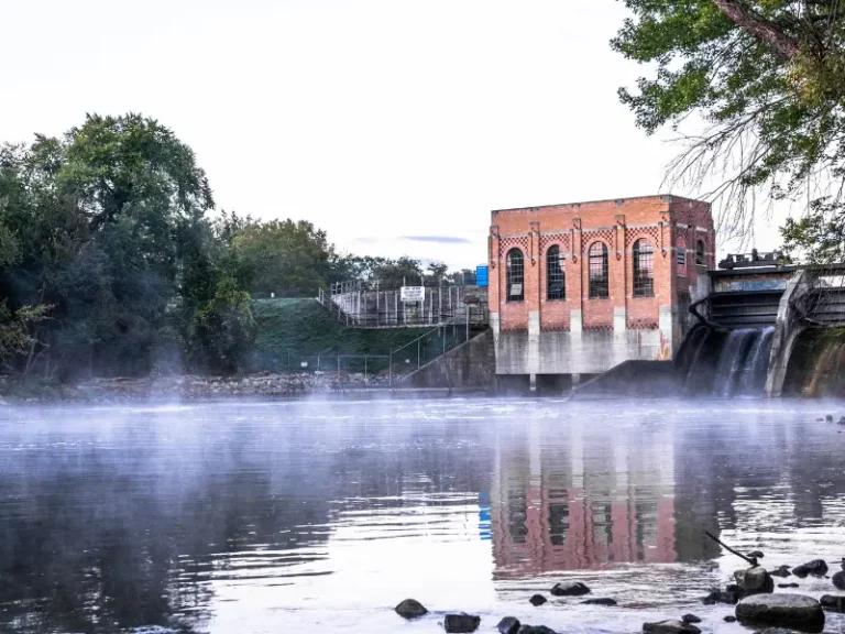 Brick hydroelectric dam building with water flowing and mist over the river at dawn.