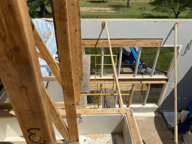 Wooden framing and scaffolding inside a house under construction with a large window opening.